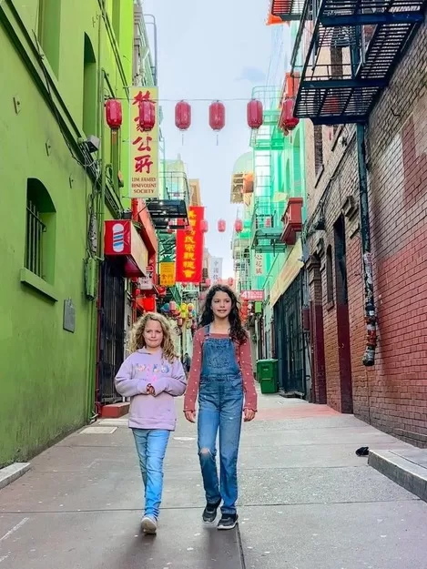 During 4 Days in Northern California with kids these two girls are walking down a Chinatown alleyway in San Francisco