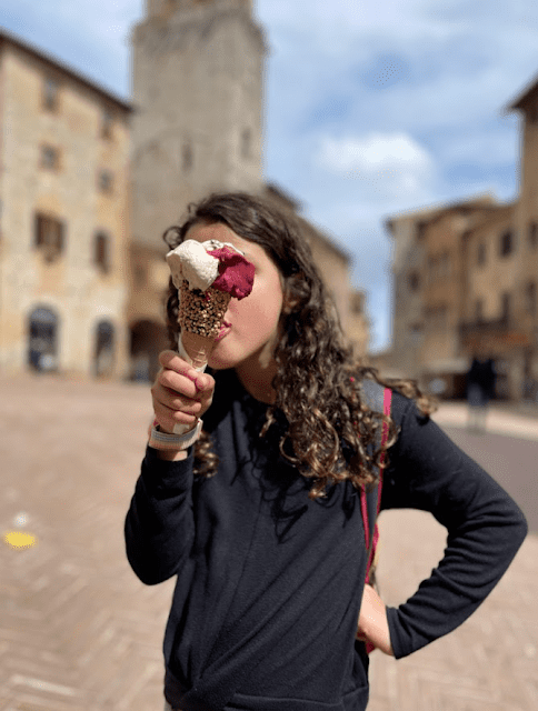 Gelato is always the answer when traveling in Tuscany with kids. A little dark haired girl enjoys a cone of gelato in an Italian village