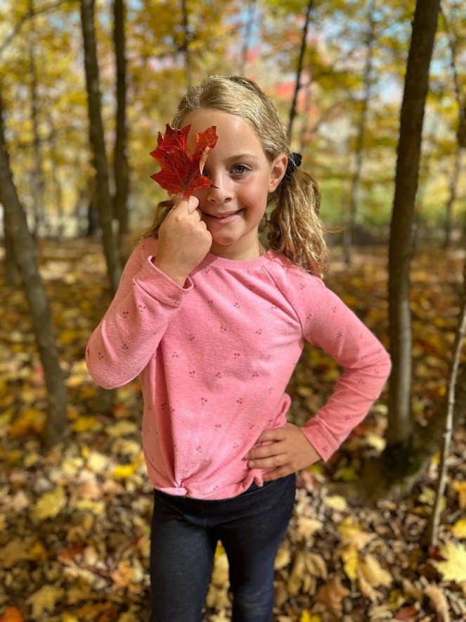 Little girl poses with a red leaf over her eye when in the catskills in the fall