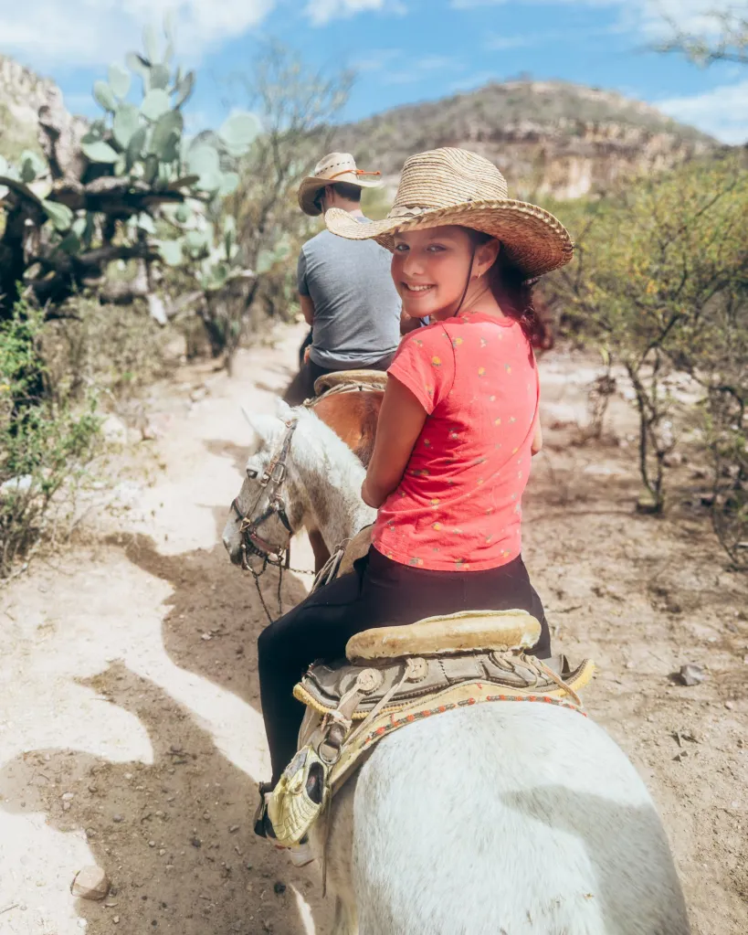 Little girl in a cowboy hat looking over her shoulder while riding a horsenat Xotolar Ranch