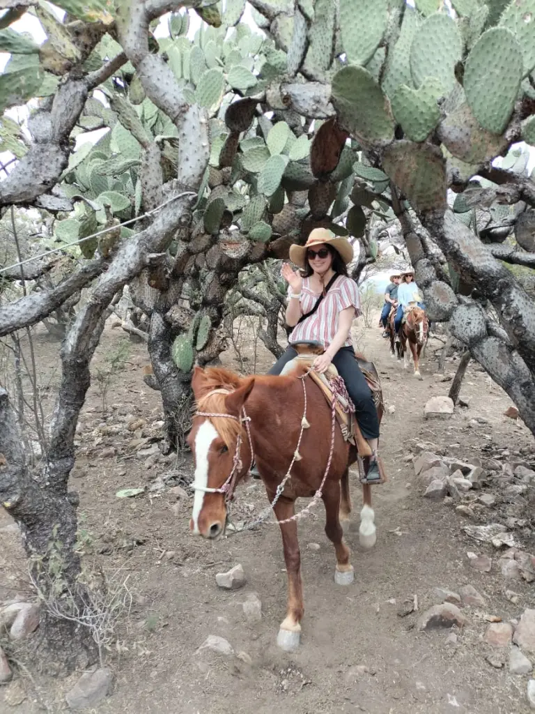 Lindsey from Adventurous Tastes waving on horseback as she rides through cacti on Xotolar Ranch near San Miguel de Allende