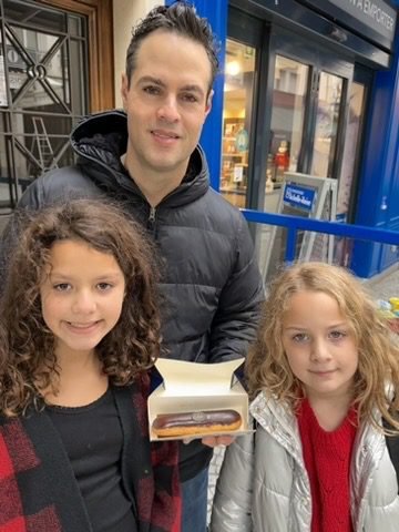 Man and two daughters posing for a photo with an eclair in Paris