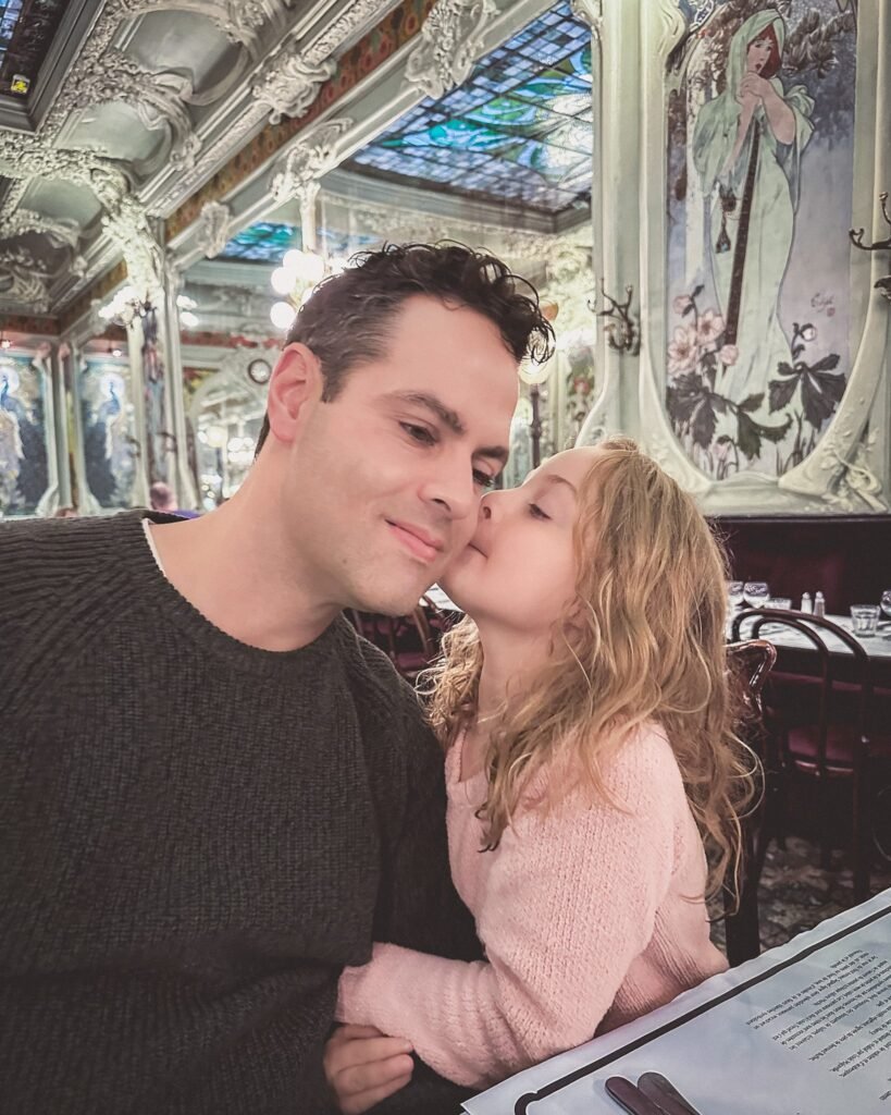 Blond little girl kissing her dark haired father on the cheek at Bouillon Julian