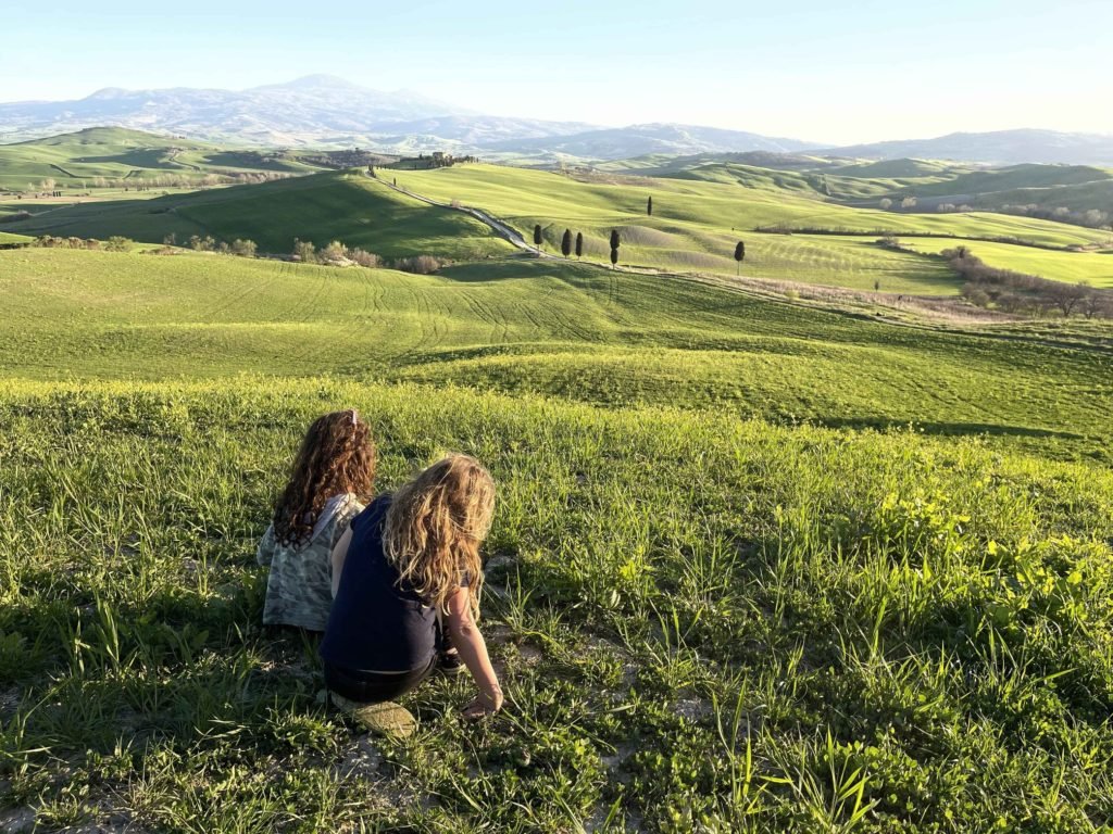 Two girls sitting on a field in Tuscany, one of the best places to consort in Europe for families