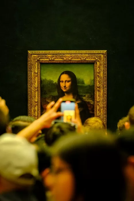 A crowd of people at the Louvre admiring the Mona Lisa - close up of heads and hands holding cell phones to take photos of the painting.