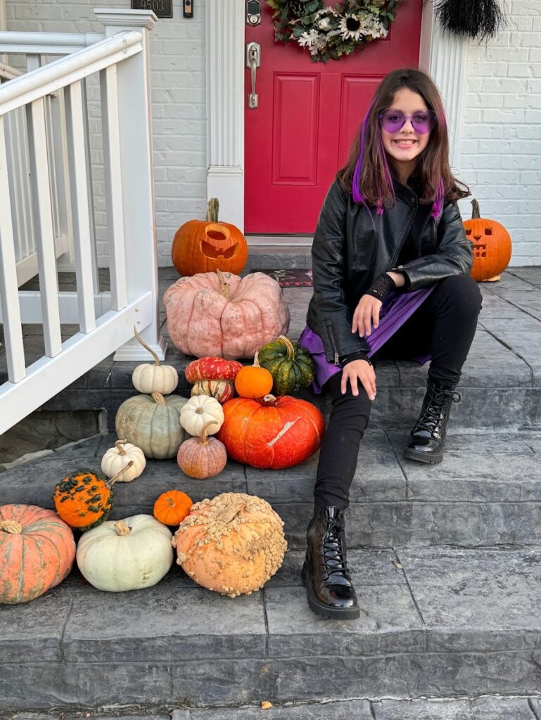 Front porch and red front door with pumpkins and little girl posing in Halloween costumes