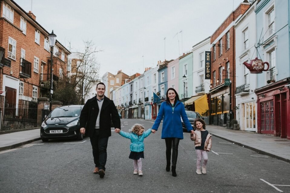 Family holding hands and walking down the middle of the street in Notting Hill, London, in front of brightly colored home